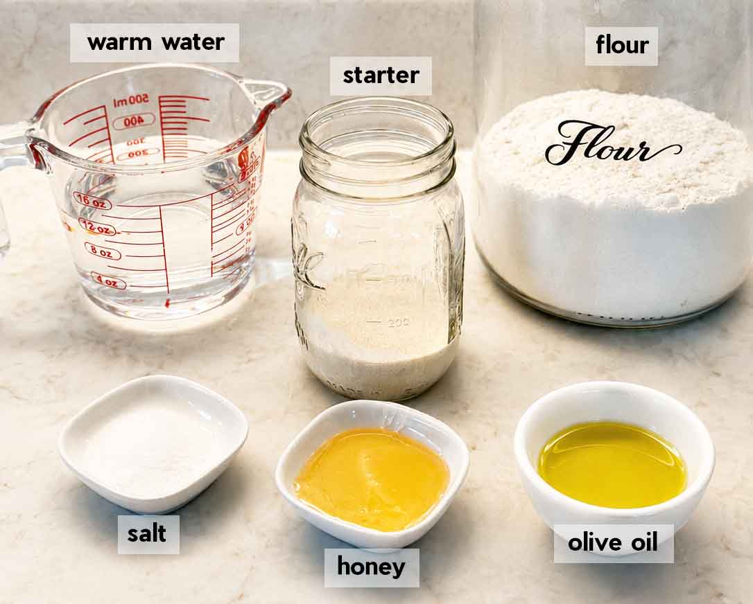 Labeled ingredients for sourdough pizza dough: warm water, active sourdough starter, bread flour, salt, honey, and olive oil