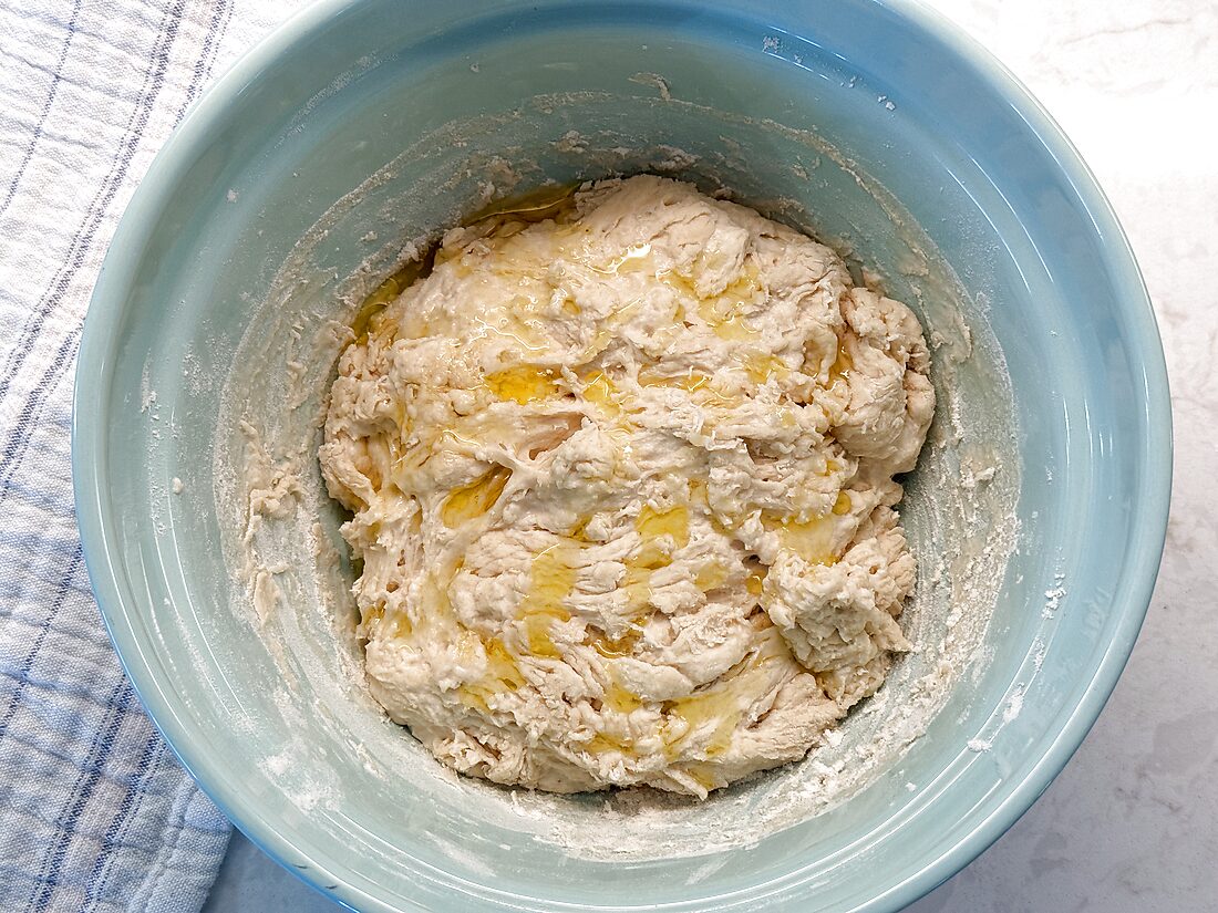 Olive oil being worked into sourdough pizza dough by folding it over itself by hand