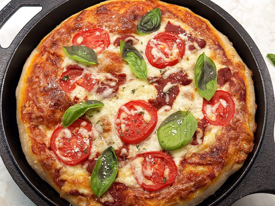 Sourdough pizza dough recipe baked into a deep dish cast iron pizza topped with mozzarella, tomatoes, and fresh basil