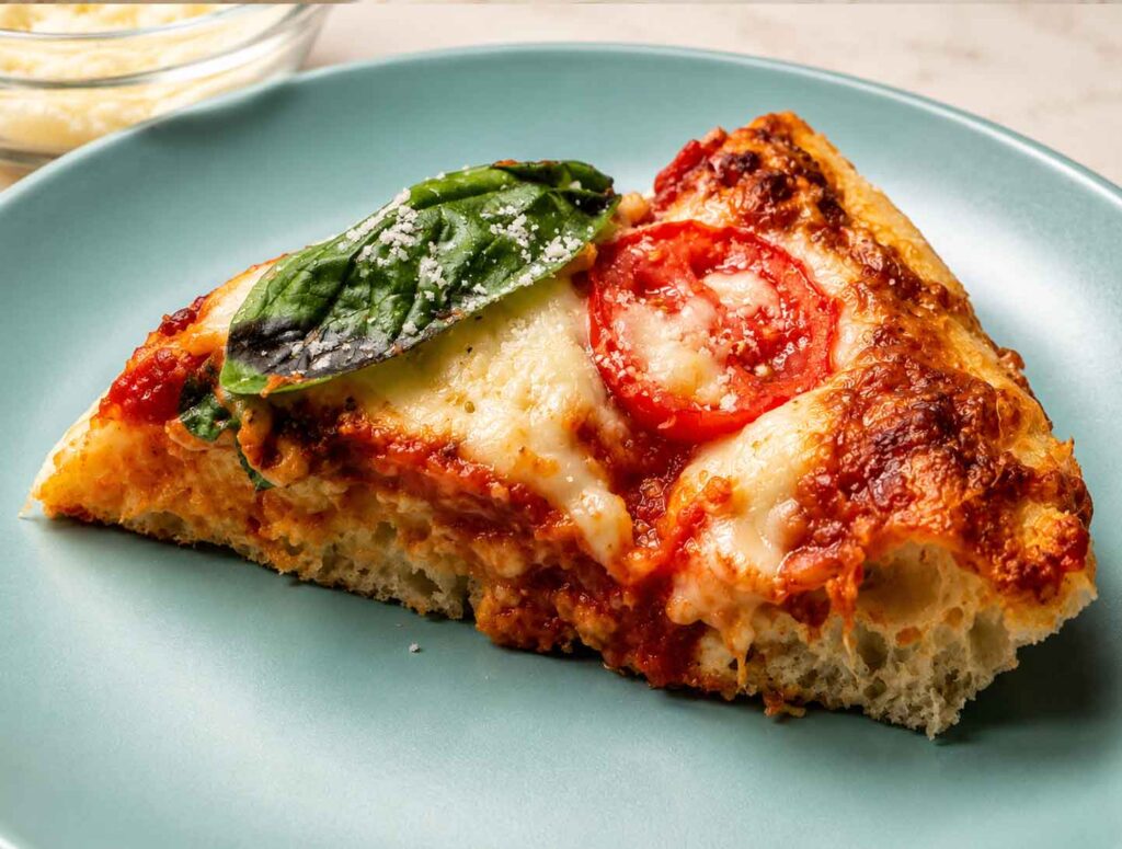 Slice of sourdough pizza on a blue plate topped with mozzarella, tomatoes, and fresh basil