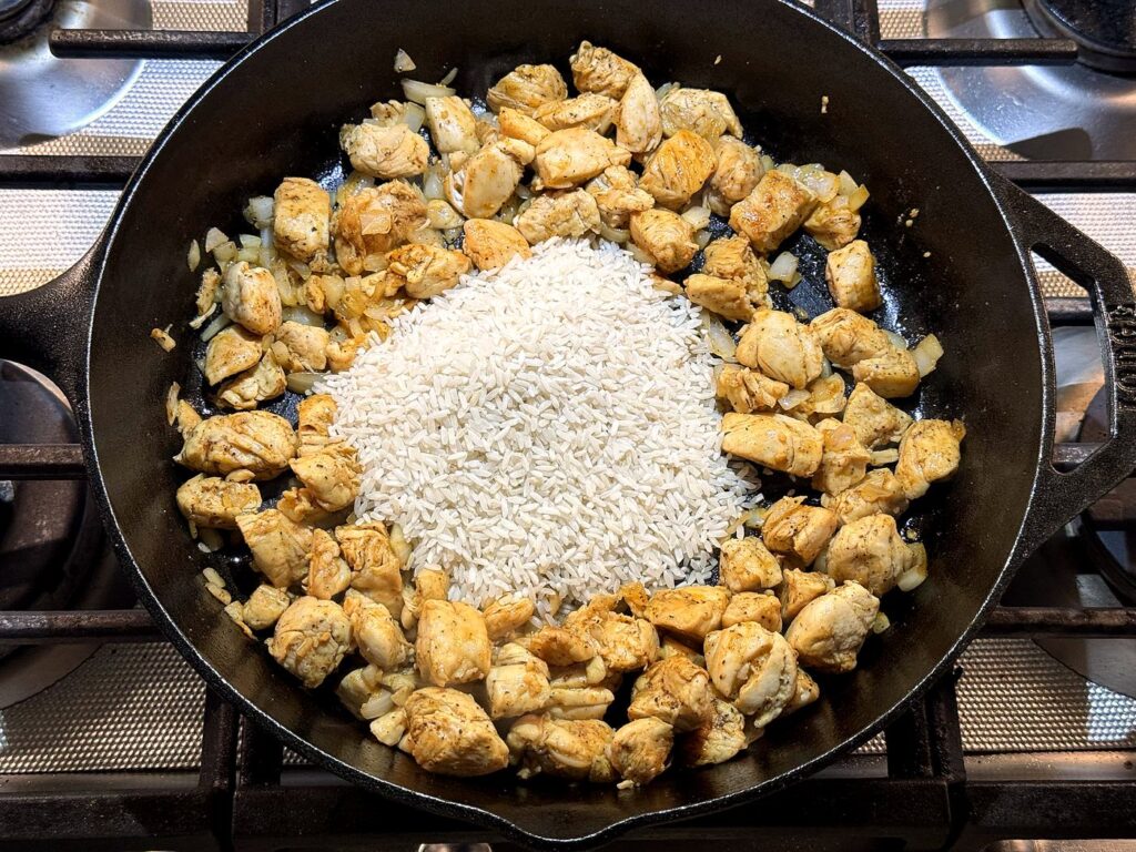 Uncooked white rice stirred into the chicken and onion in the skillet.