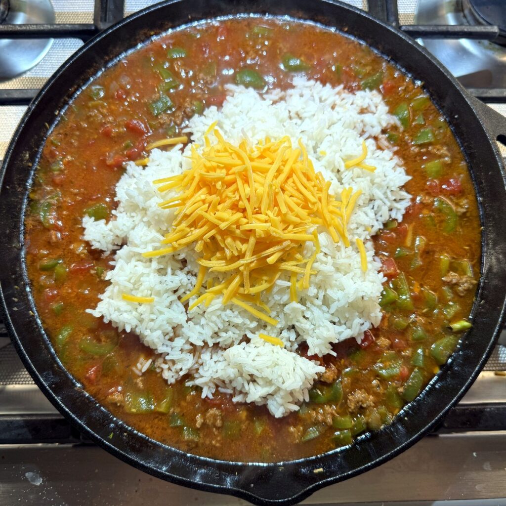 Cooked white rice and shredded cheddar added to the tomato and beef mixture in the skillet before stirring.