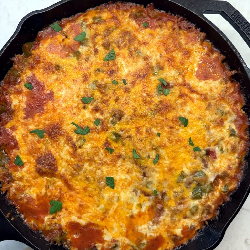 Baked stuffed pepper casserole in a cast iron skillet, topped with melted cheddar and mozzarella and a sprinkle of parsley.