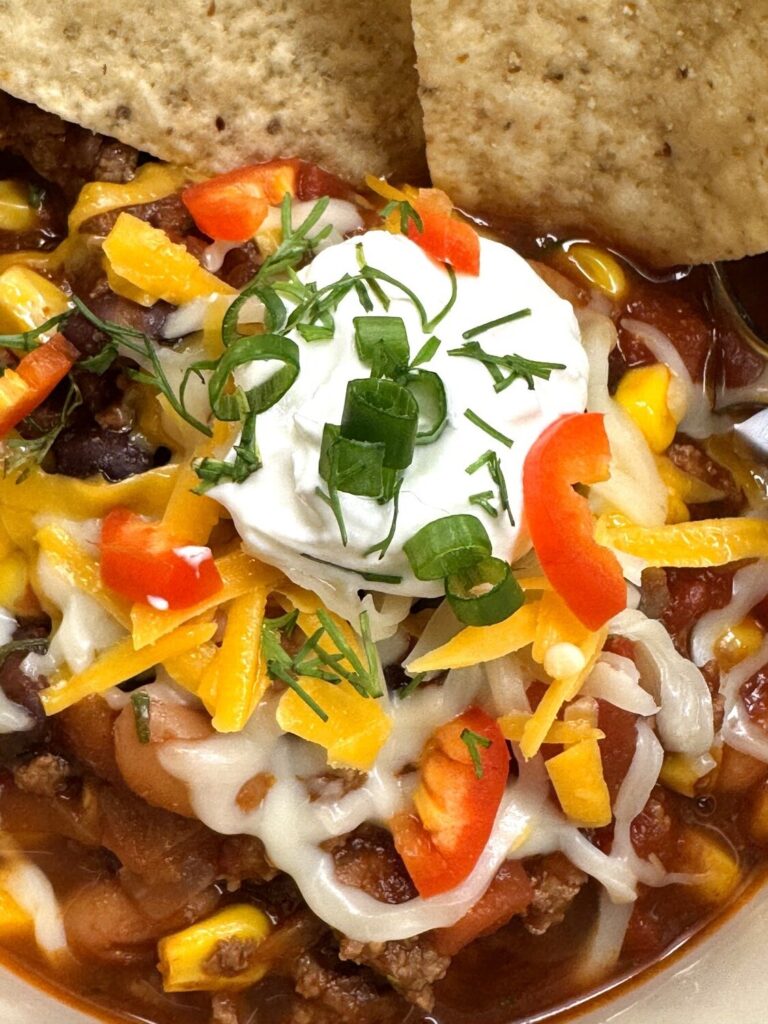 Close-up of taco soup topped with sour cream, shredded cheese, red pepper, and green onion