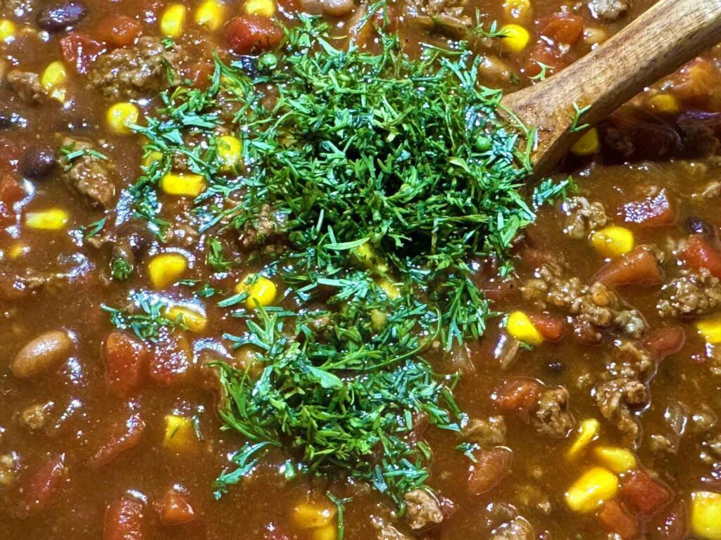 Fresh chopped cilantro being stirred into a pot of taco soup