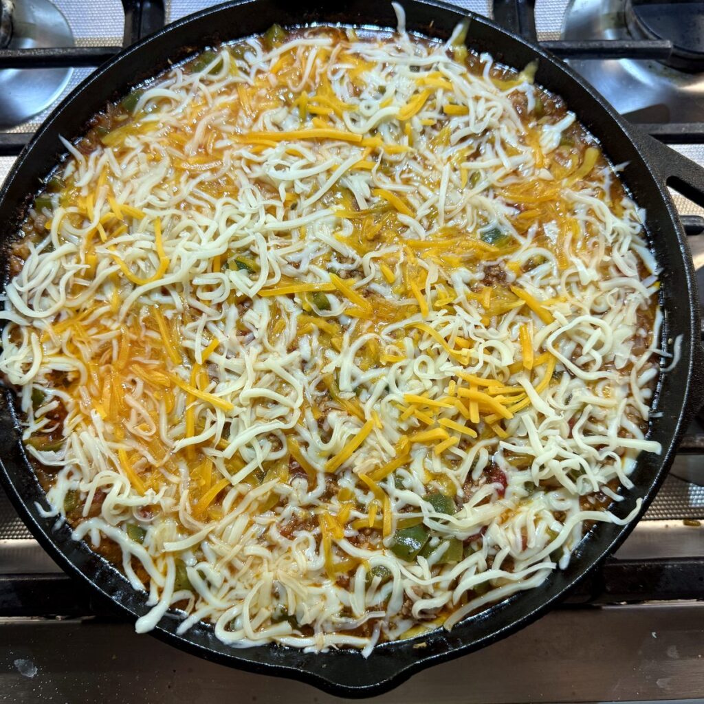 Shredded cheddar and mozzarella scattered over the top of the stuffed pepper casserole in the skillet before baking.