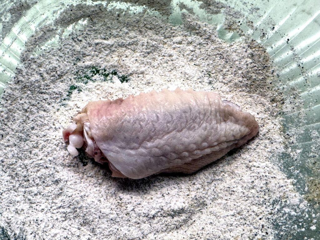 A chicken wing being coated in baking powder and seasoning