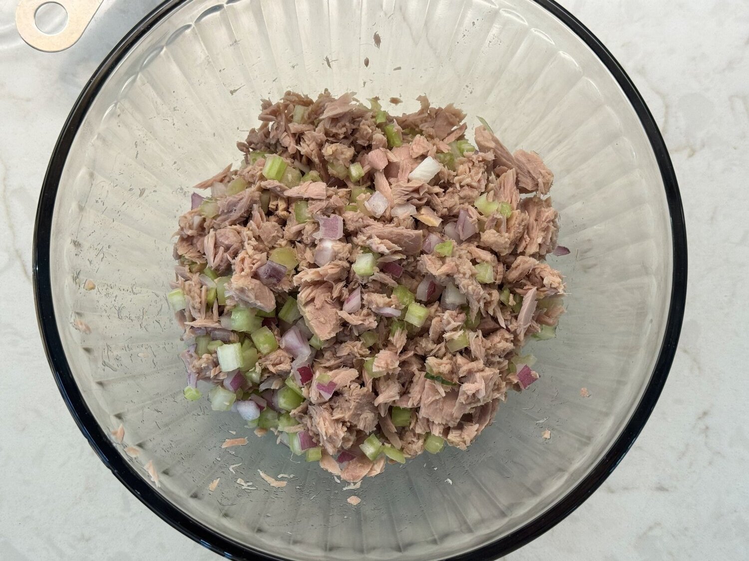 Diced celery and red onion being folded into creamy tuna salad