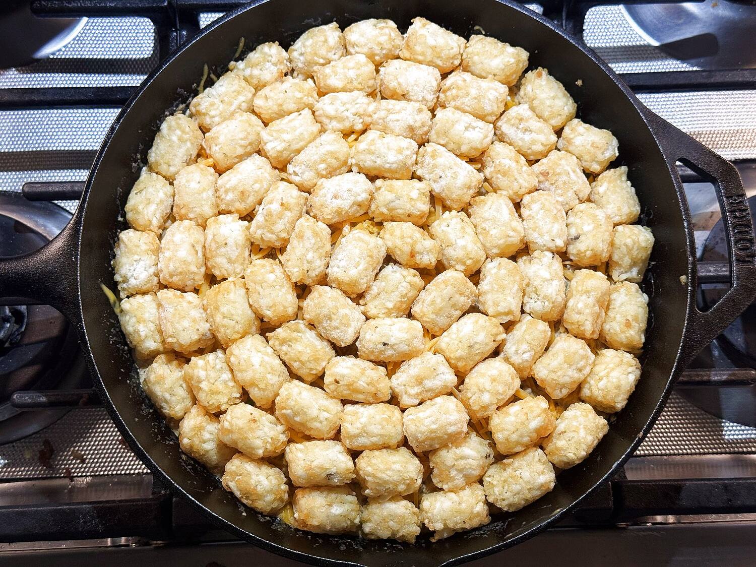 Frozen tater tots arranged in a single layer over the creamy beef filling in a cast iron skillet.