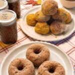 Baked pumpkin doughnuts coated in cinnamon sugar, stacked on a white plate beside a mug of coffee