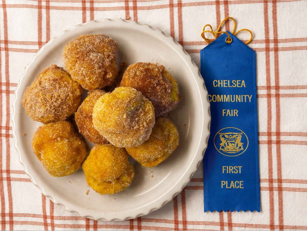 A place of cinnamon sugar pumpkin doughnut holes with a Chelsea Community Fair blue first place ribbon