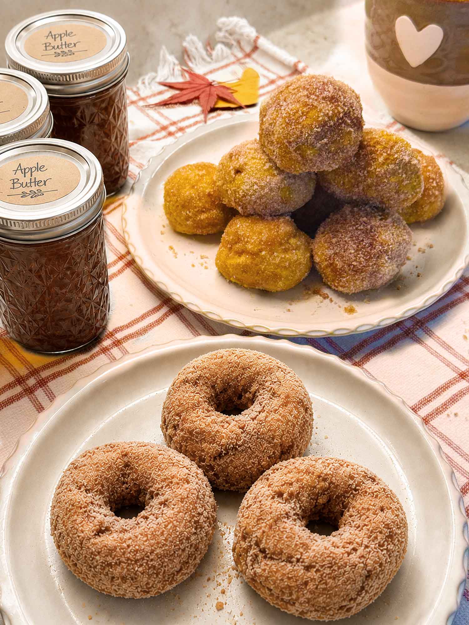 Baked pumpkin doughnuts coated in cinnamon sugar, stacked on a white plate beside a mug of coffee