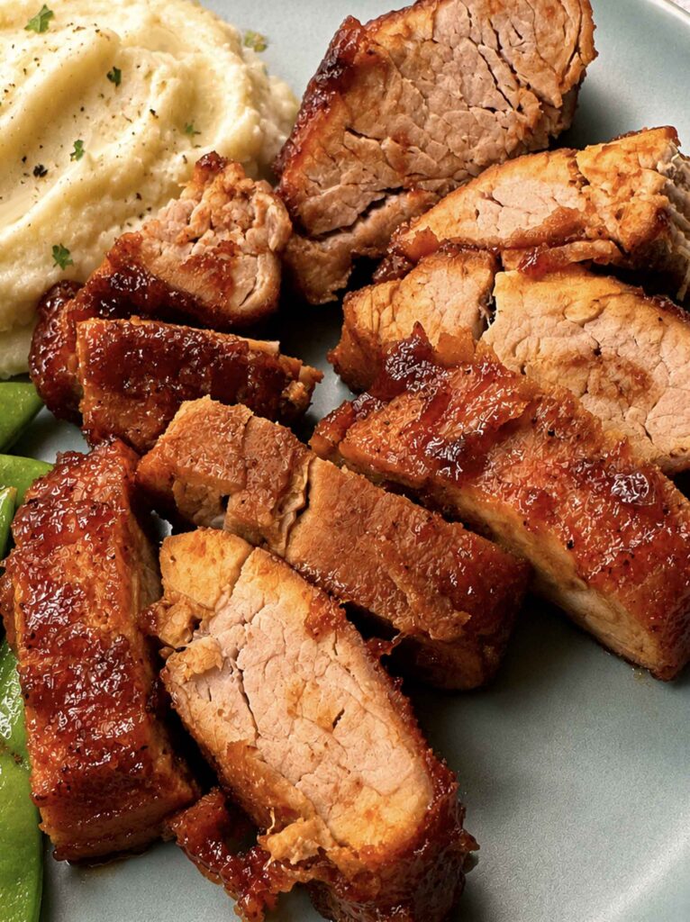 Brown sugar BBQ pork tenderloin sliced into glazed medallions on a plate with mashed potatoes