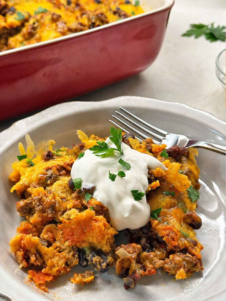 Serving beef enchilada casserole with sour cream and parsley