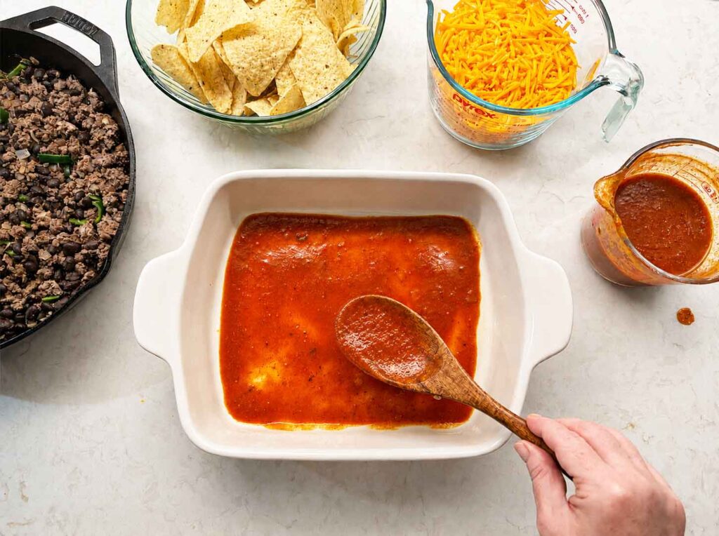 Layering the beef enchilada casserole by beginning with the enchilada sauce