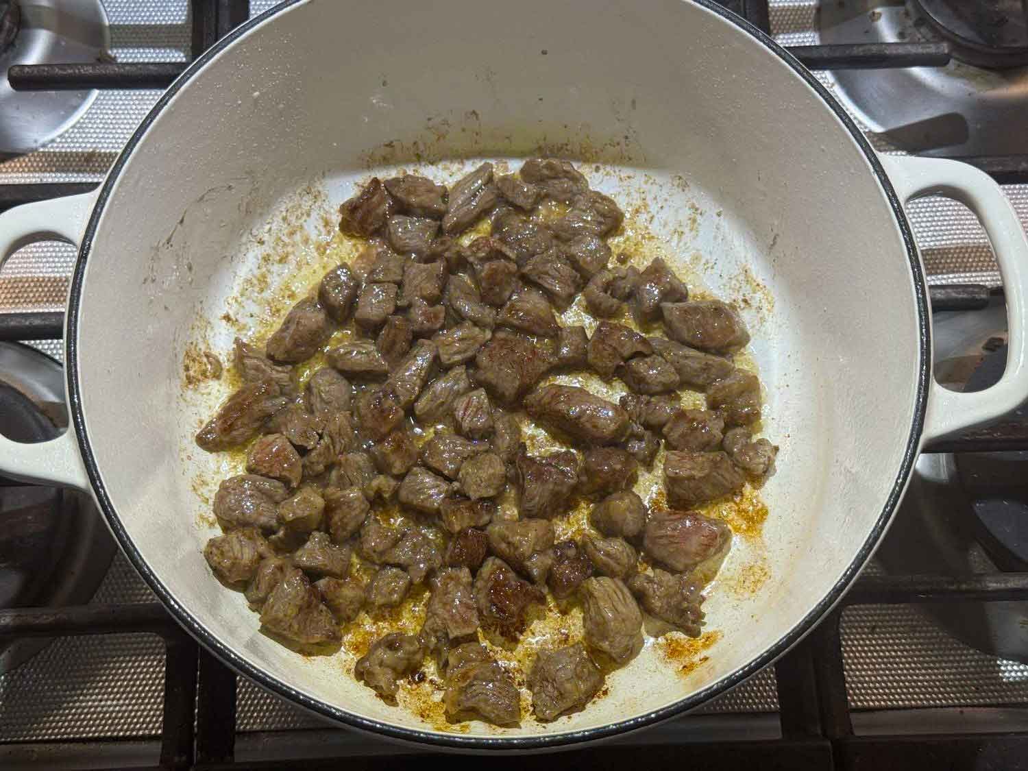 Cubes of sirloin browning in a white Dutch oven