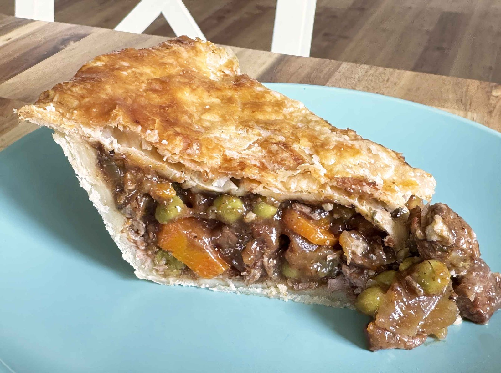 A plated slice of beef pot pie showing tender beef, carrots, peas, and gravy inside a flaky crust