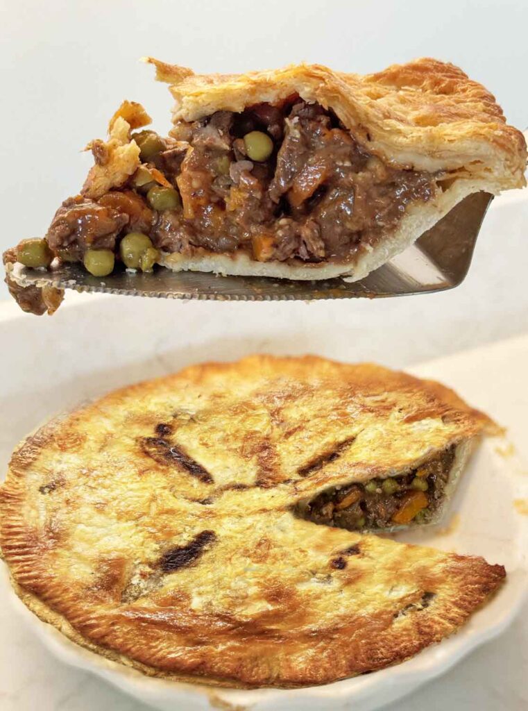 A slice of beef pot pie lifted out on a server, showing beef, peas, and gravy under a flaky crust