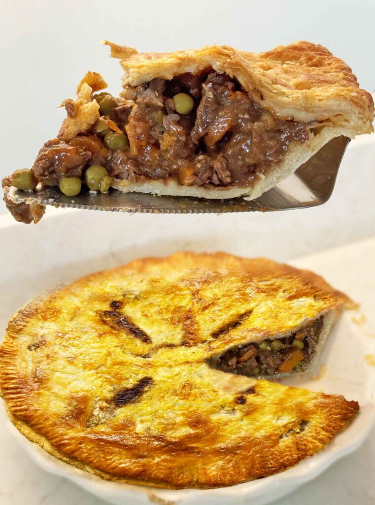 A slice of beef pot pie lifted out on a server, showing beef, peas, and gravy under a flaky crust