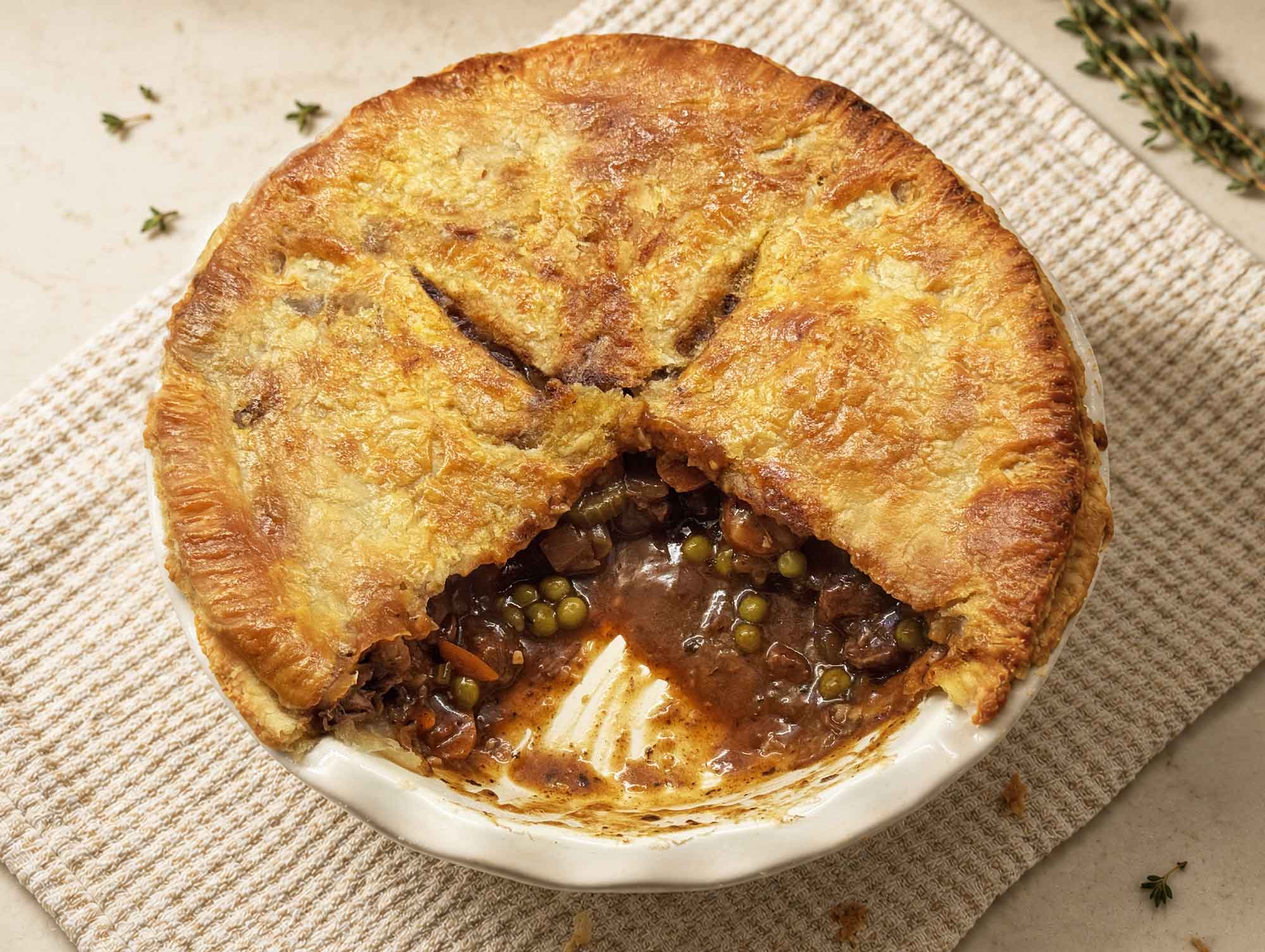 Overhead view of a homemade beef pot pie with one slice removed, showing the beef and pea filling