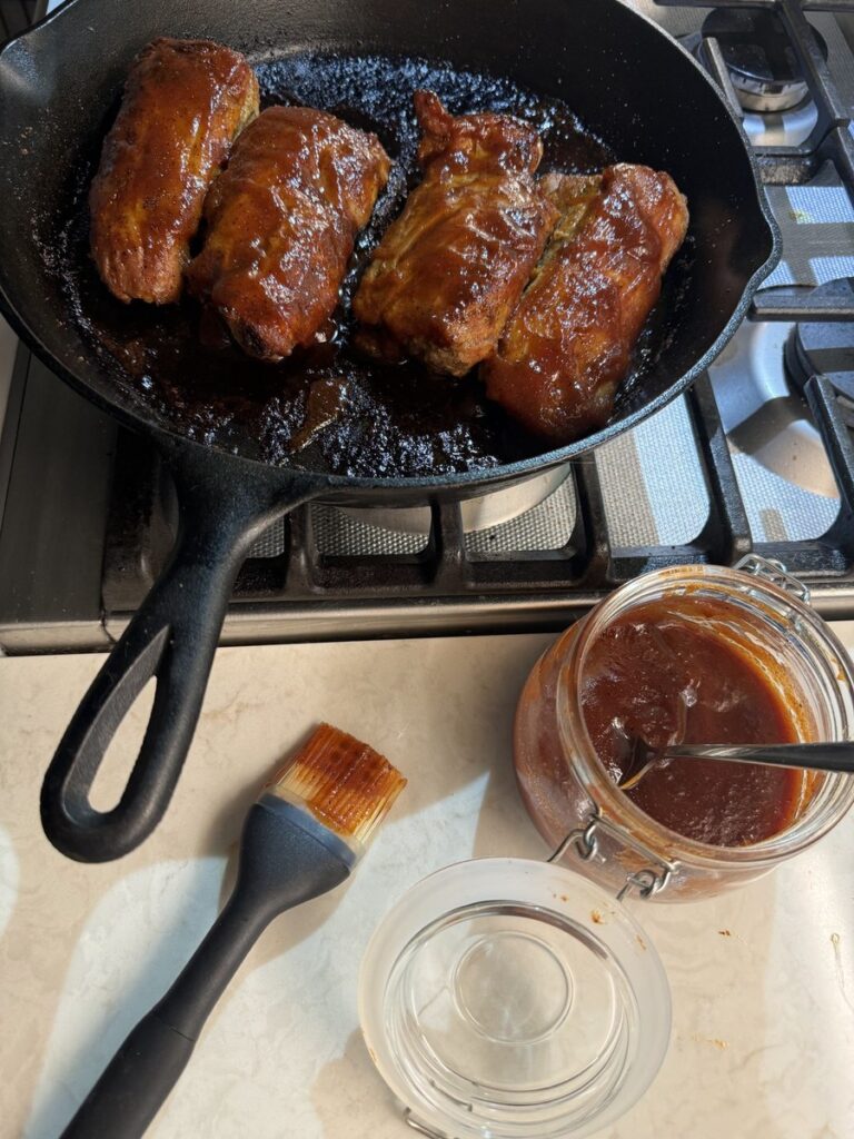 Brushing barbecue sauce over a roasted pork tenderloin in a skillet