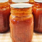 A jar of home-canned spaghetti sauce with meat on a gingham cloth