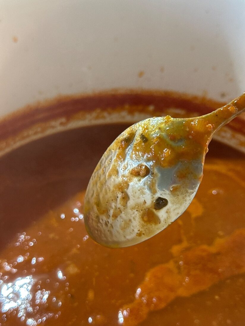 A spoon lifted from the pot showing the meat sauce coating the back of it