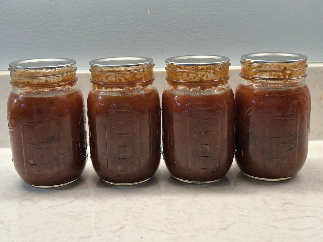 Sealed jars of spaghetti sauce with meat cooling on a folded towel on the counter