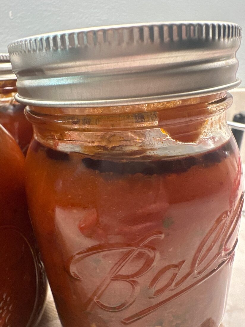 A jar of just-canned spaghetti sauce showing a dark line at the top of the sauce