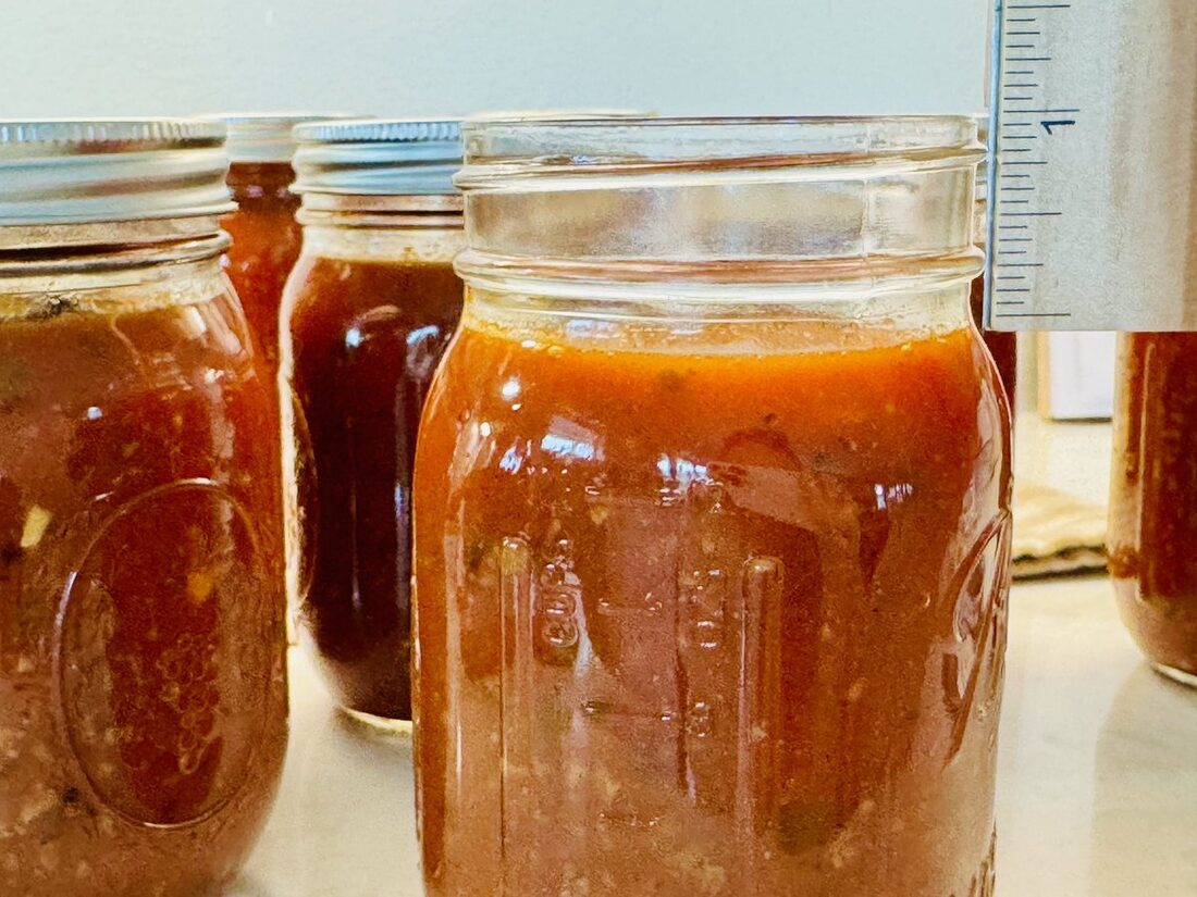 A filled jar of spaghetti sauce with a ruler measuring 1 inch of headspace at the top