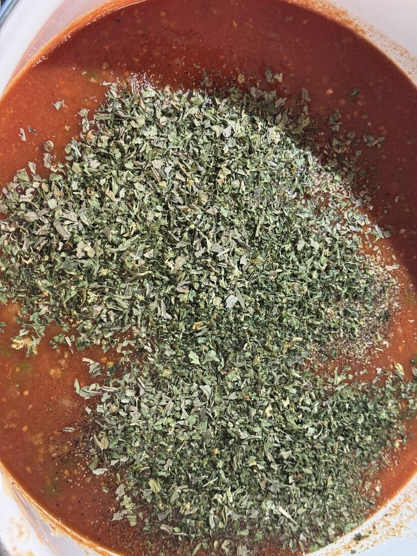 Dried herbs piled on top of the tomato and meat sauce in the pot before stirring in