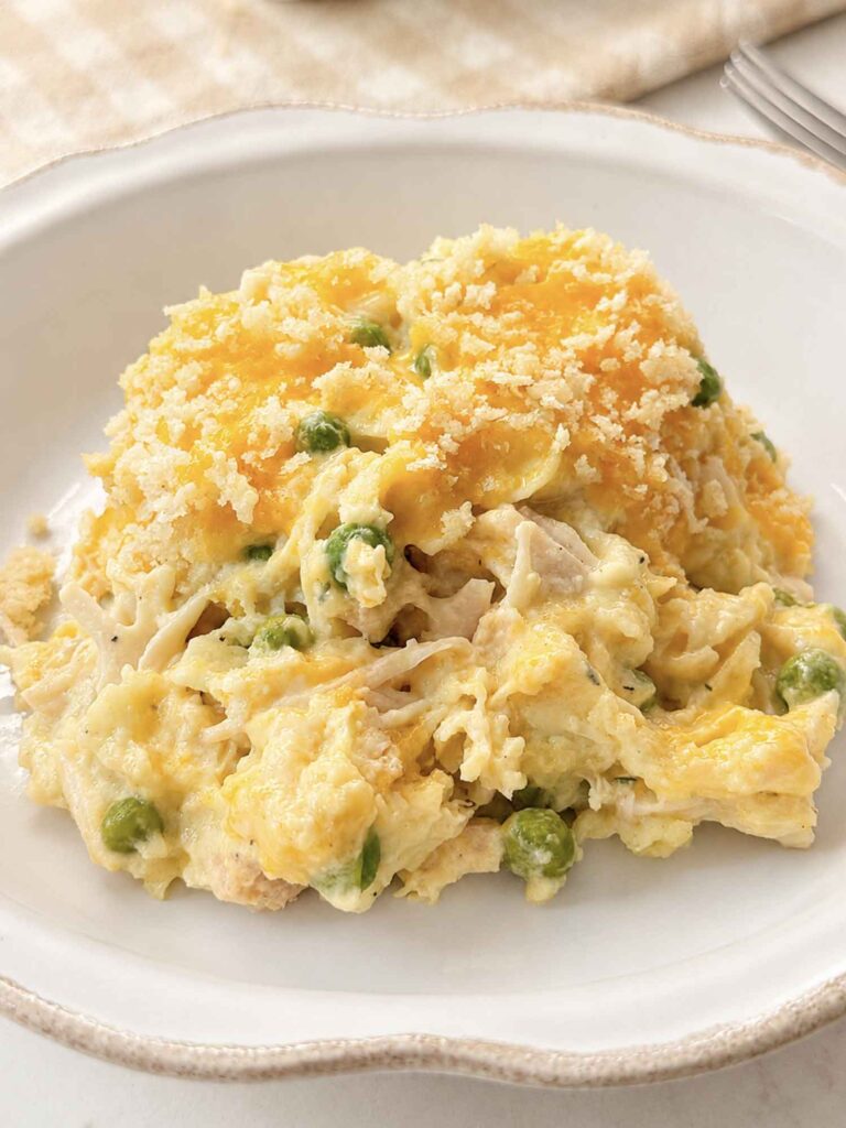 A bowl of creamy chicken noodle casserole with peas and a golden panko topping