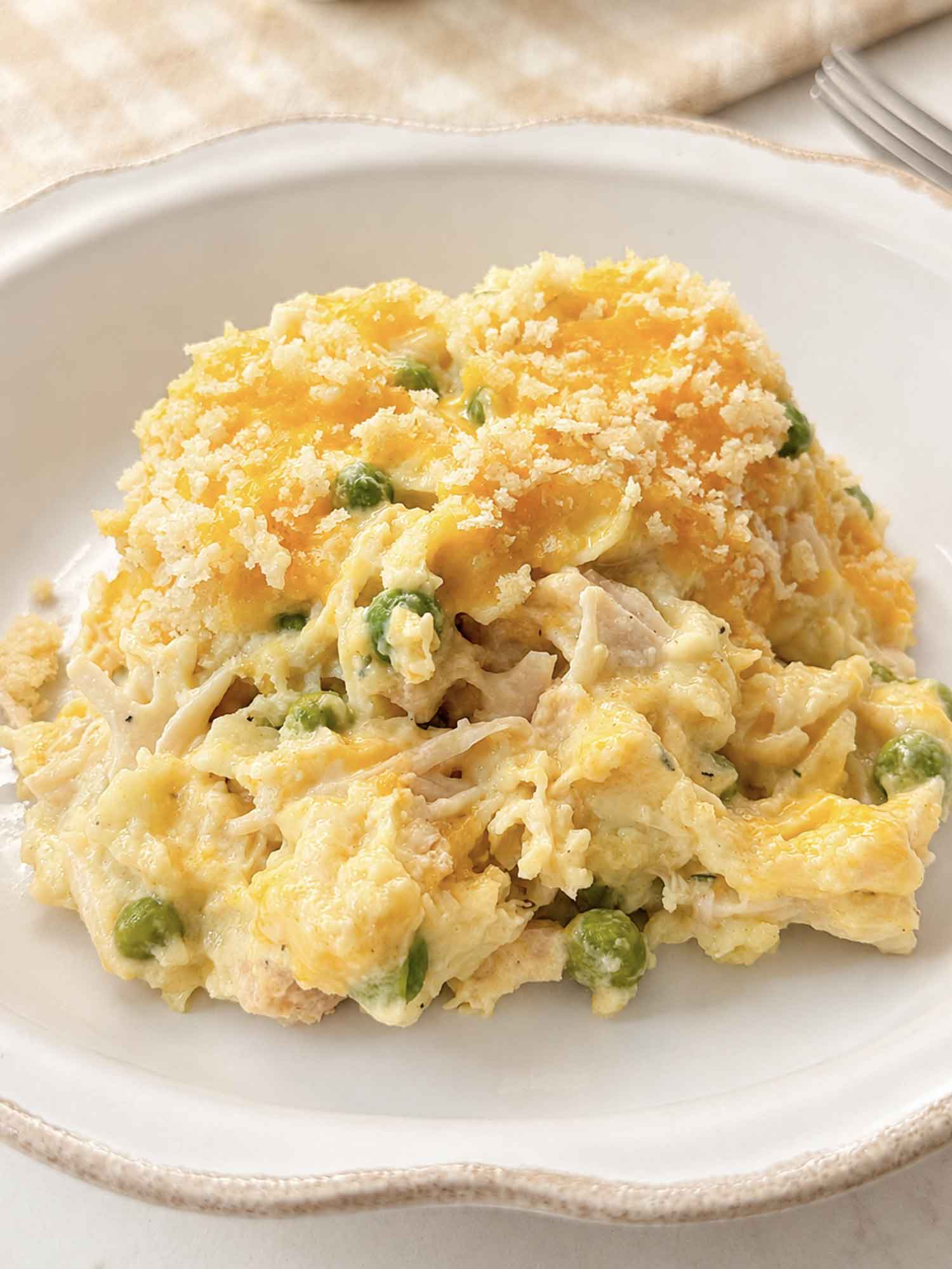 A bowl of creamy chicken noodle casserole with peas and a golden panko topping