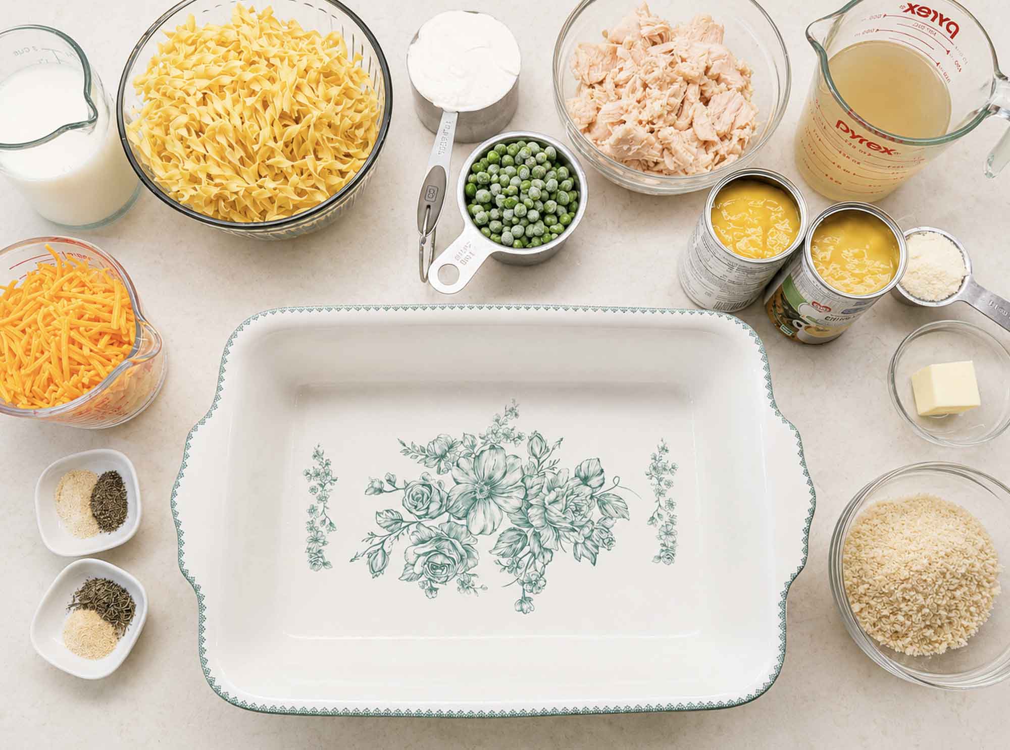 Chicken noodle casserole ingredients arranged around an empty white 9x13 baking dish