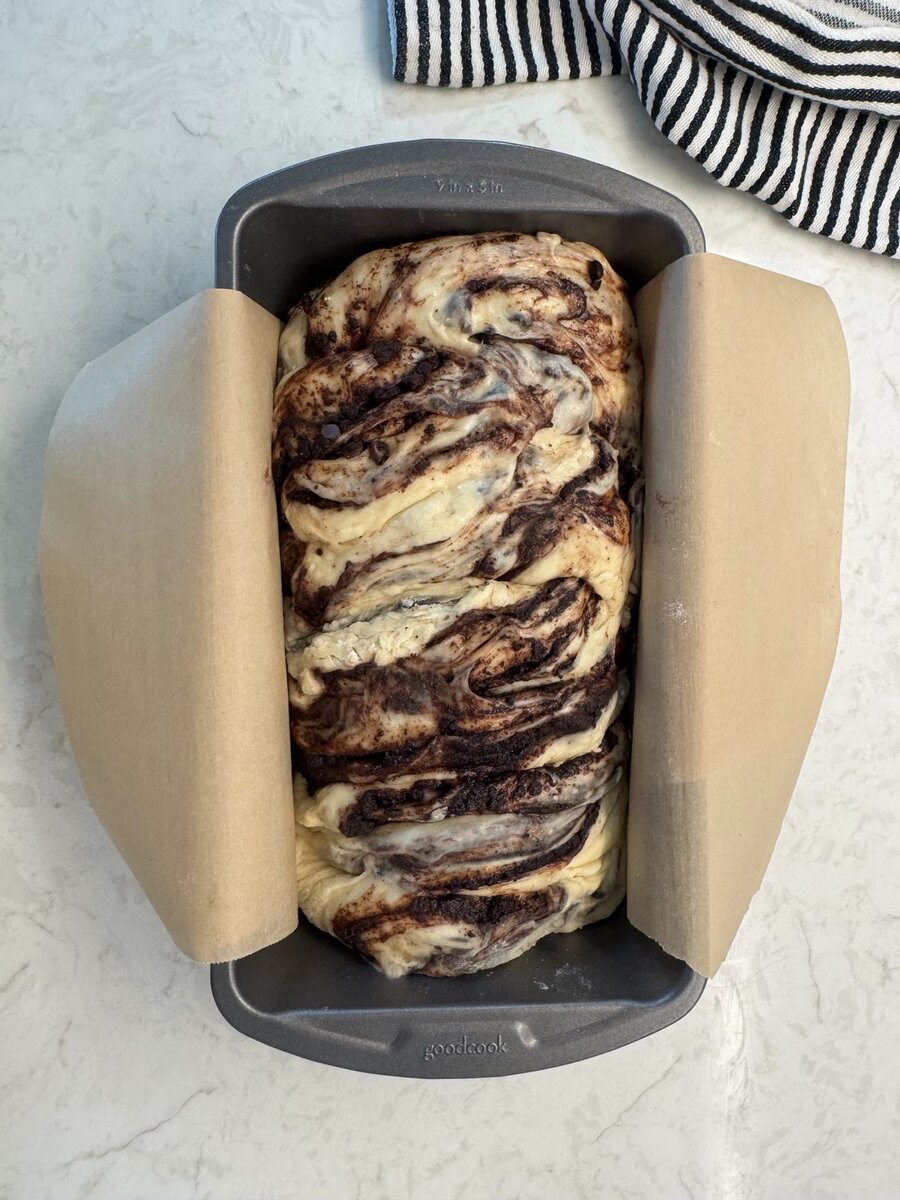 Twisted and braided chocolate babka dough in a parchment-lined loaf pan
