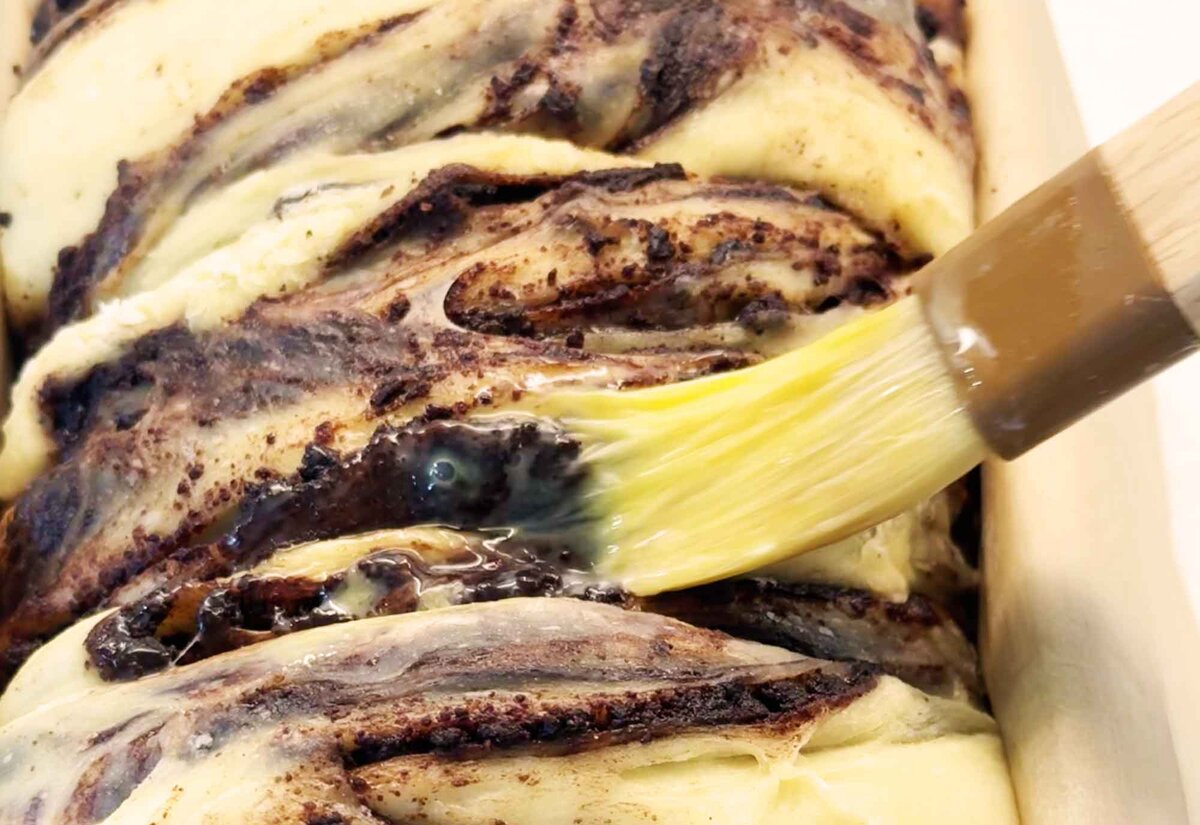 Brushing egg wash over the risen chocolate babka before baking