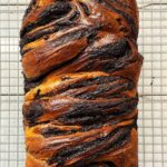 A loaf of sourdough chocolate babka cooling on a wire rack