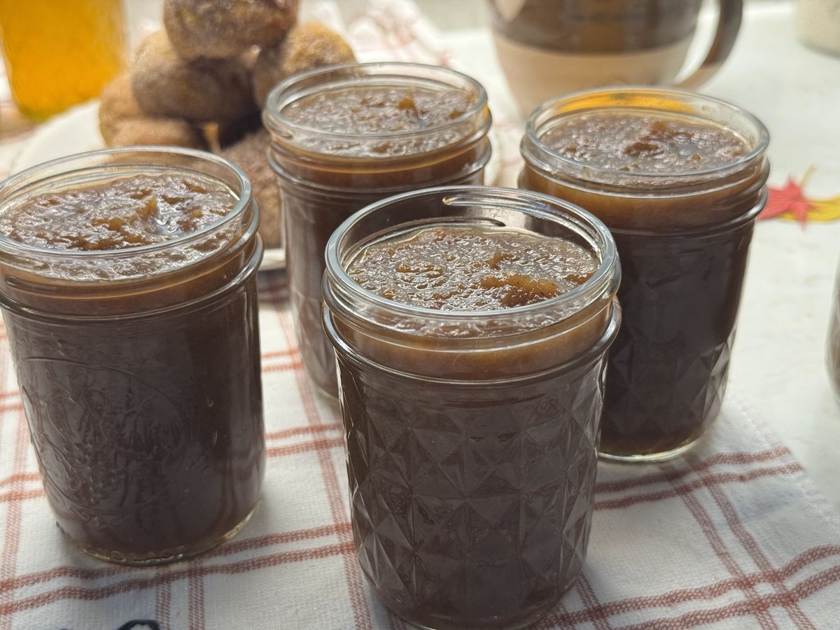 Filled half-pint jars of homemade apple butter cooling on a red and white plaid towel