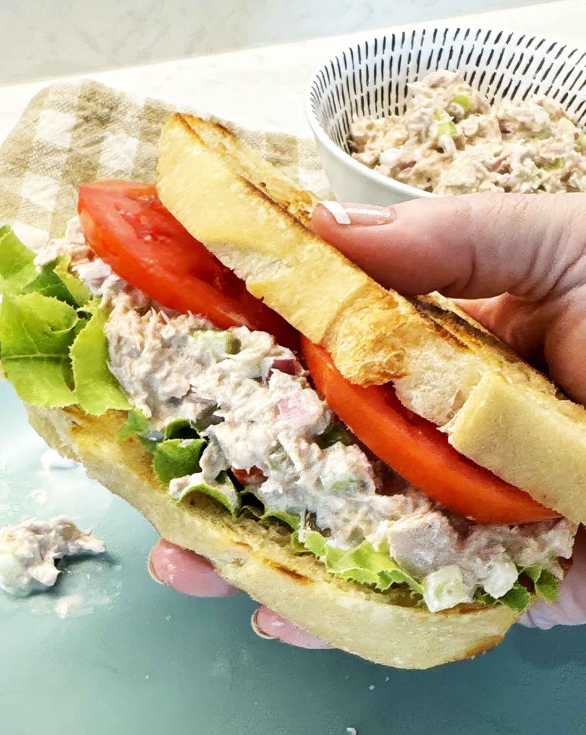 Hand holding a tuna salad sandwich on toasted sourdough with lettuce and tomato