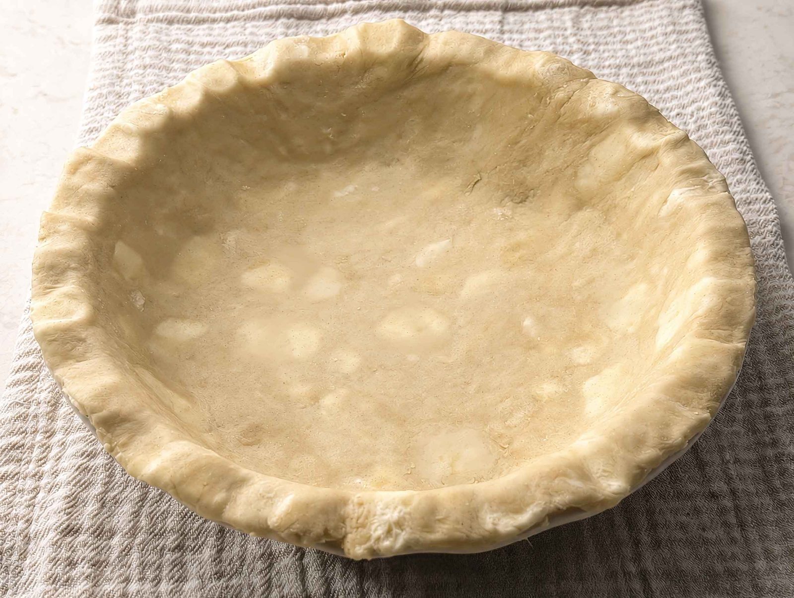 Homemade raw pie crust in a white dish showing flecks of butter throughout the dough
