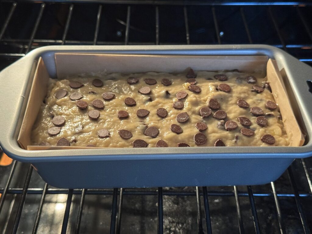 Chocolate chip banana bread loaf pan going into the oven on the center rack to bake