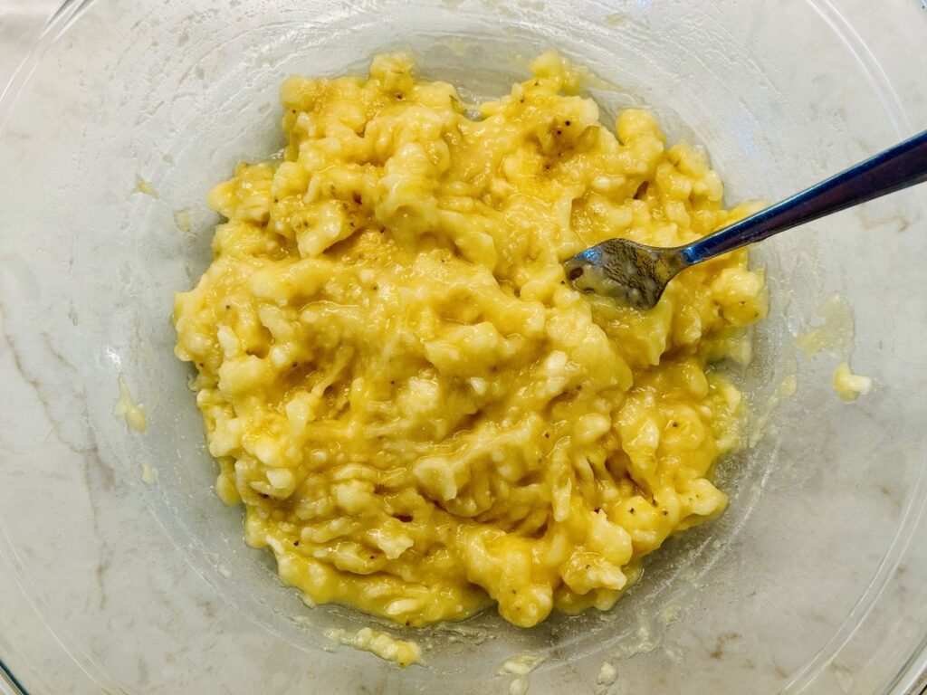 Ripe bananas mashed with a fork in a glass mixing bowl for banana bread