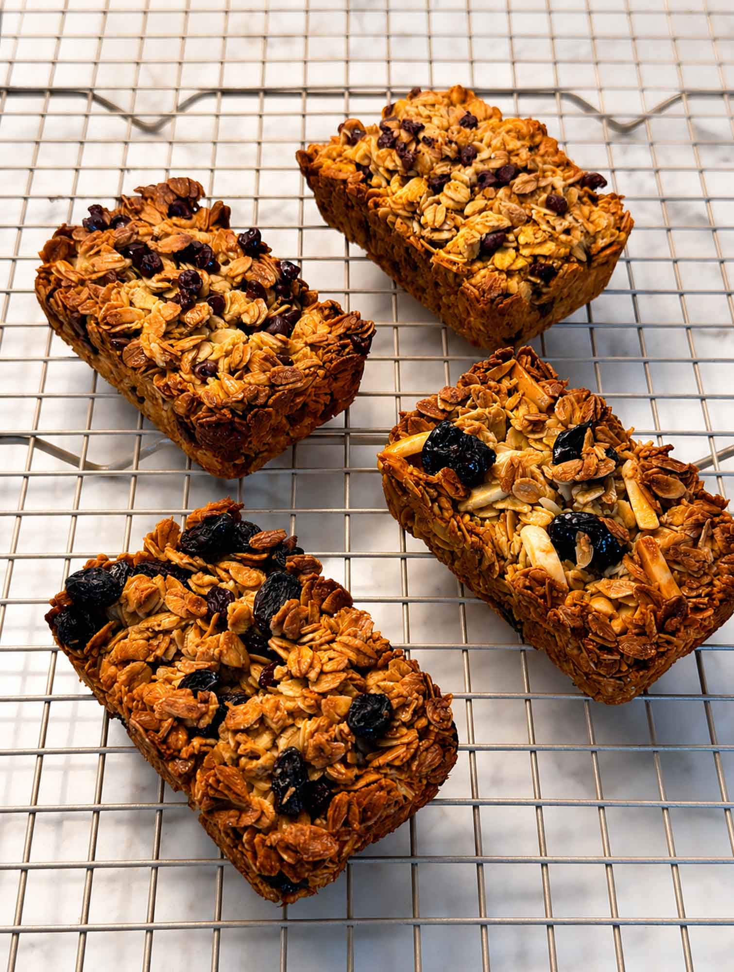 Four baked oatmeal breakfast bars in different flavors turned out onto a wire cooling rack, holding their shape.