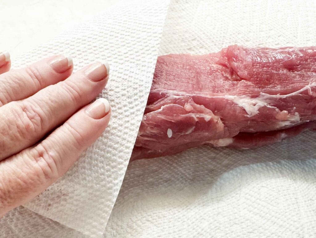Patting pork tenderloin dry with a paper towel