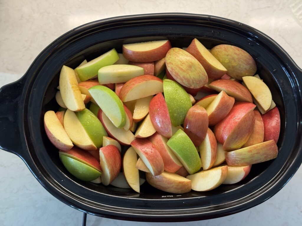 Quartered Fuji and Granny Smith apples with the skins on, filling a black slow cooker crock