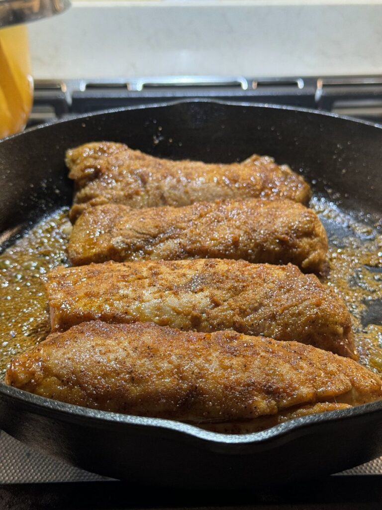 Pork tenderloin searing in a cast iron skillet with a browned crust forming