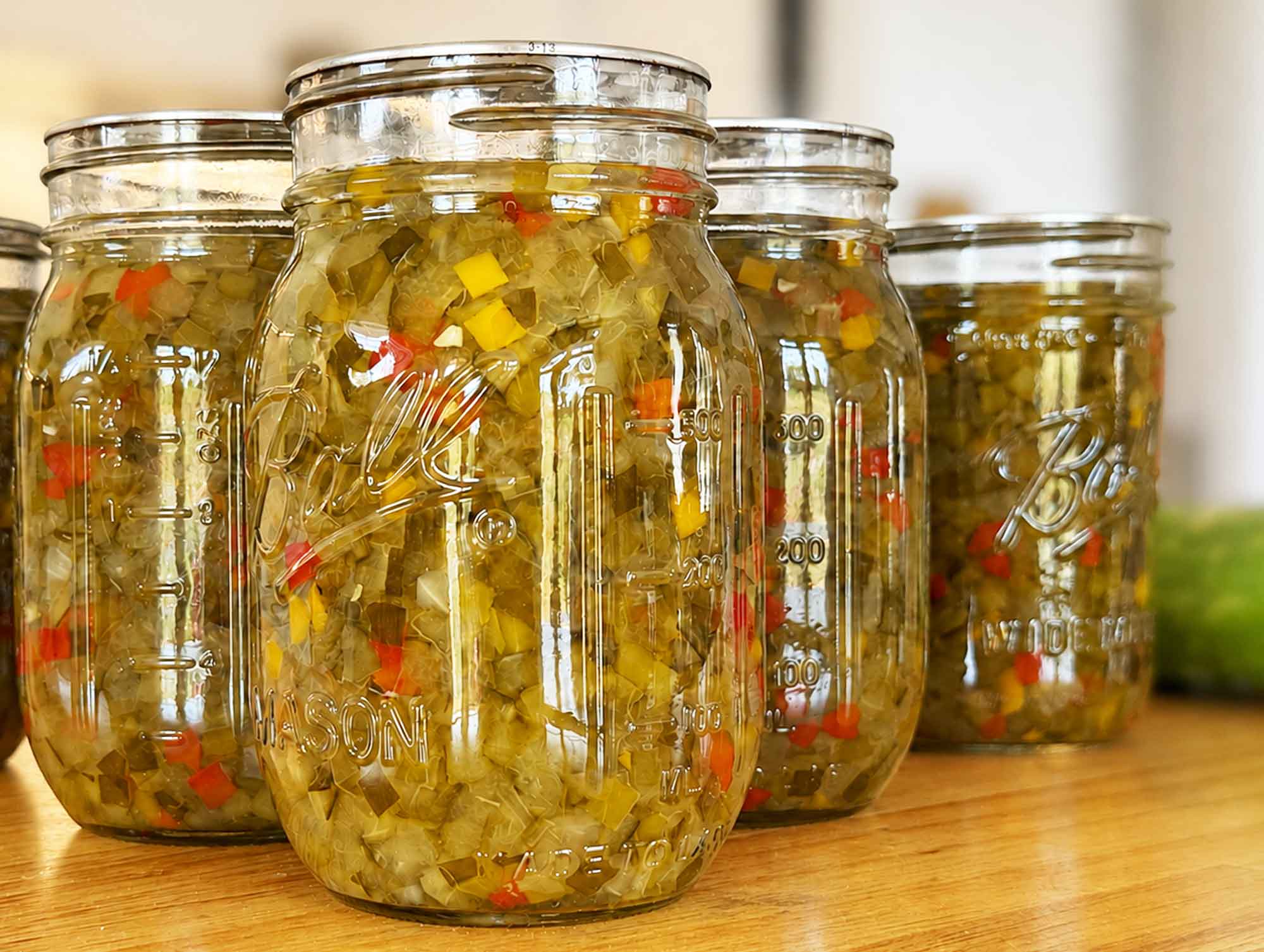 Several sealed jars of homemade sweet pickle relish lined up on a wood counter