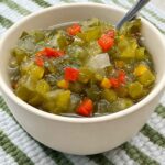 A bowl of homemade sweet pickle relish with a spoon, showing the chunky green texture and red pepper flecks