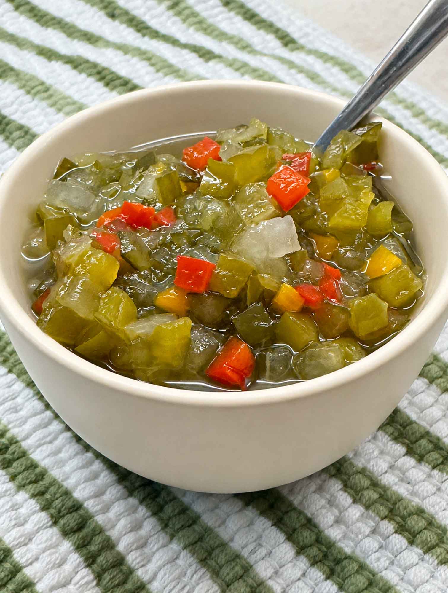 A bowl of homemade sweet pickle relish with a spoon, showing the chunky green texture and red pepper flecks
