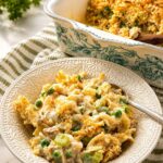 A bowl of creamy tuna noodle casserole with peas, served in front of the baking dish